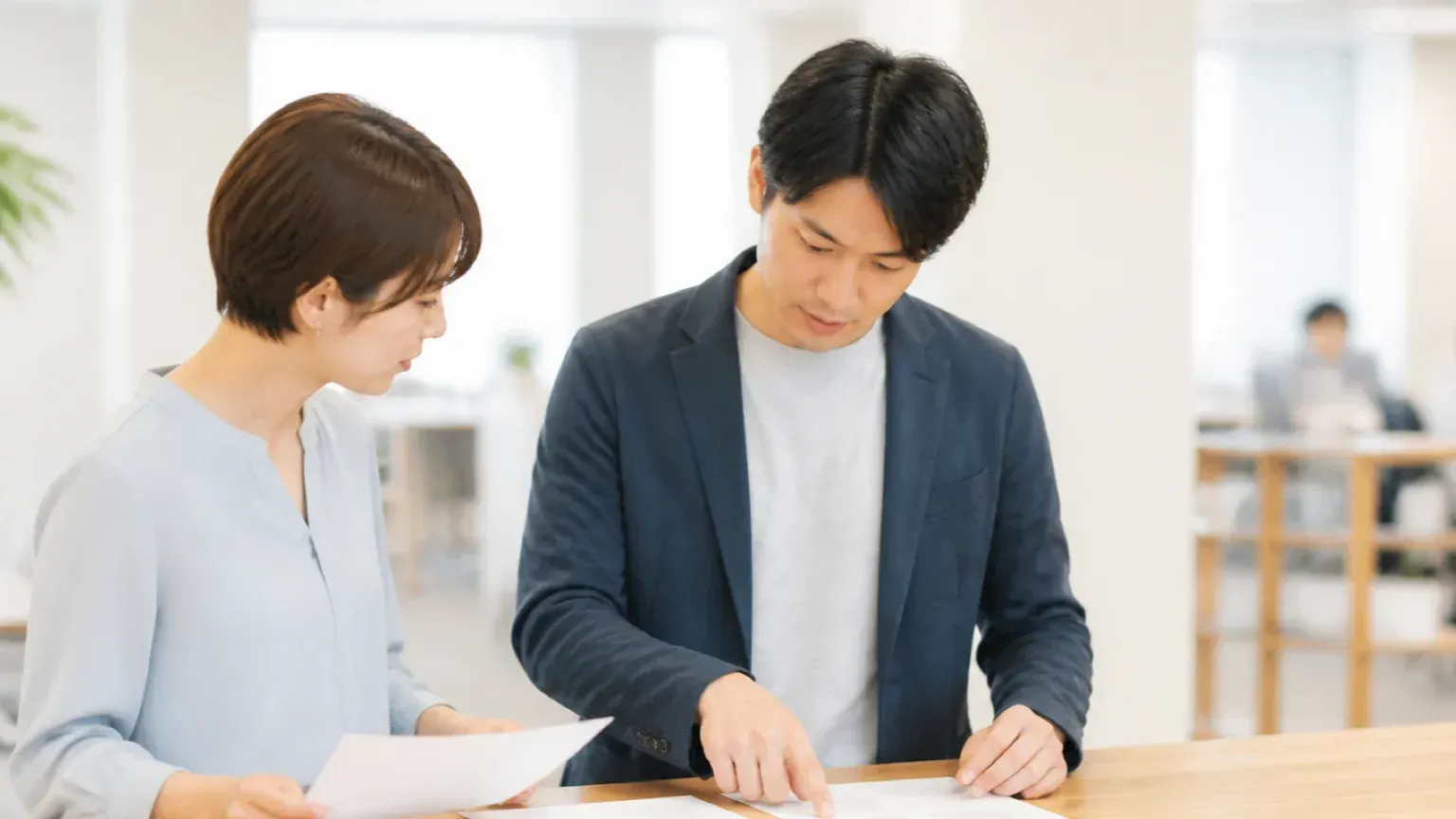 2部の見積書を並べてAI導入の費用の前提条件を突き合わせる2名の担当者