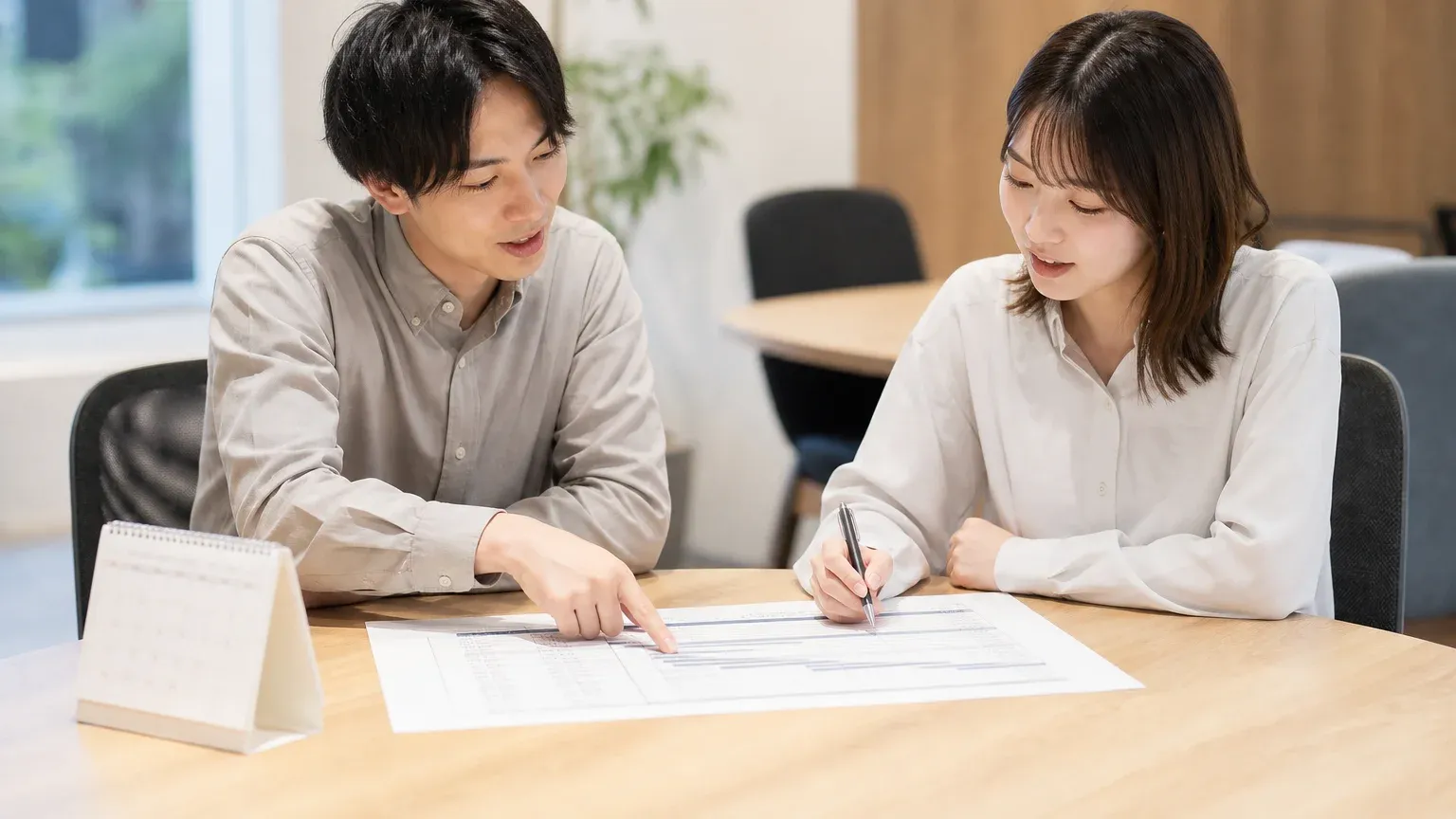 印刷した工程表と卓上カレンダーを前に、2人で構築の工程と担当・時期を決めている場面