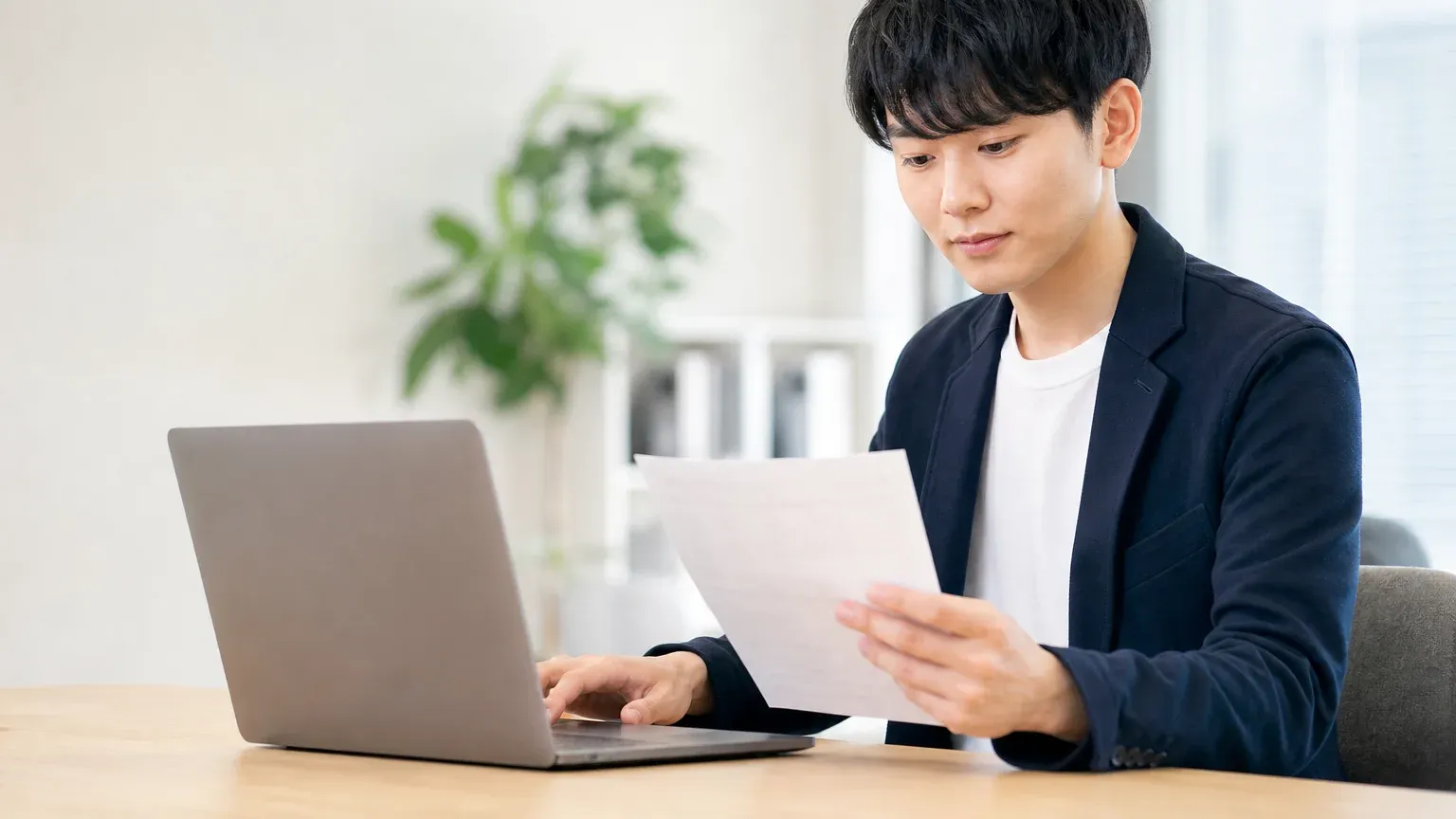 手に持った紙の伝票を見ながら、正面のノートPCへ同じ内容を入力し直している20代男性の担当者
