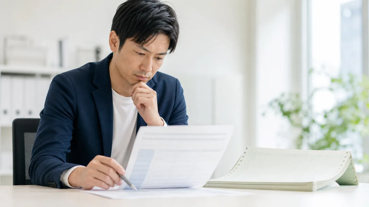 古いAS/400の帳票を見ながら基幹システムの移行方式を検討する30代の情報システム担当者