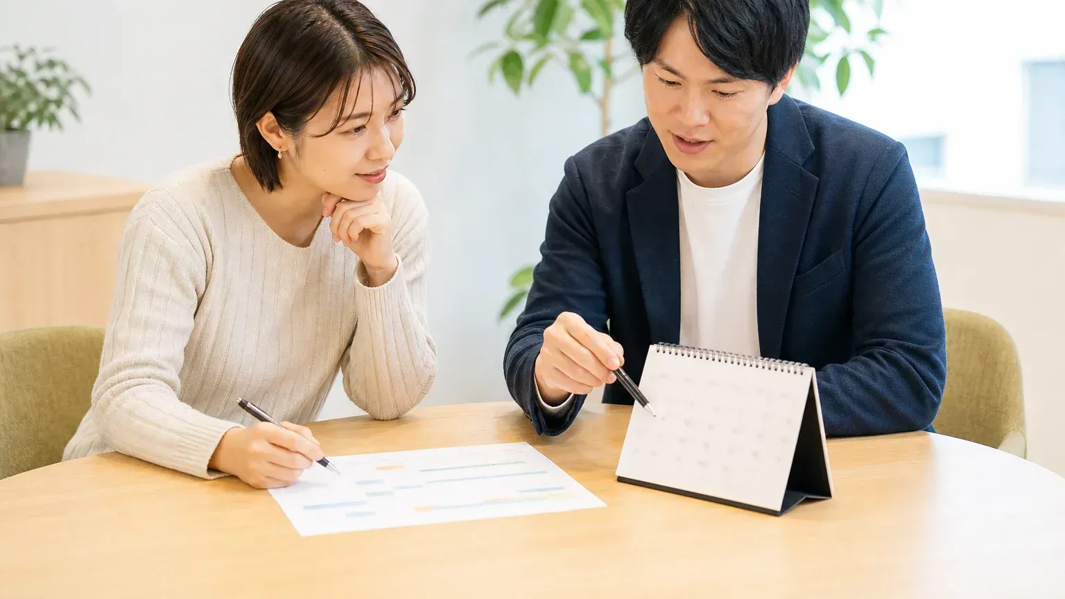 卓上カレンダーの日付をペンで指しながら、締切から逆算した期限を2人で決めている場面