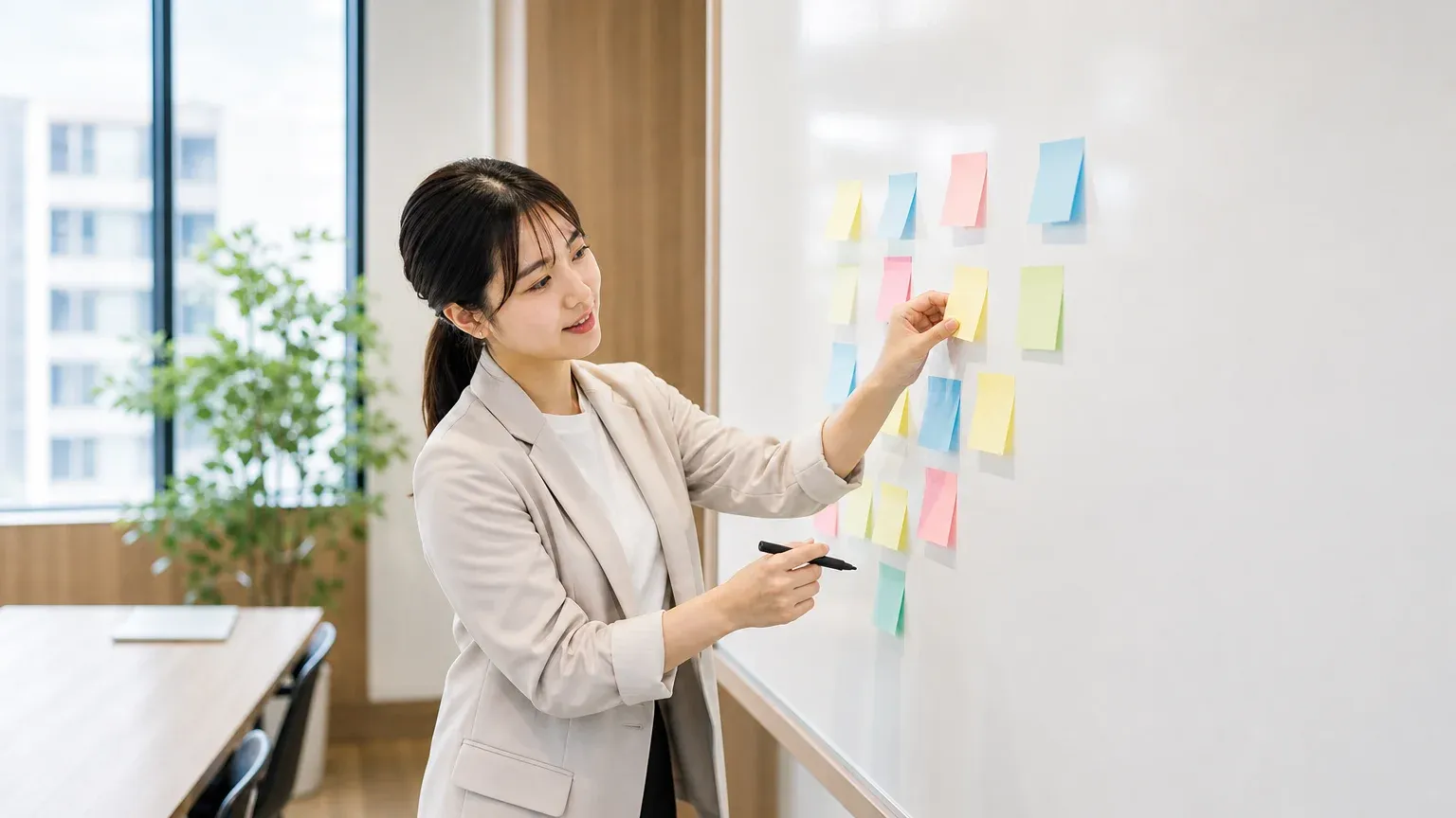 ホワイトボードに貼った付箋を並べ替えて、止まると困る業務から基幹システムの範囲を整理する20代女性の担当者