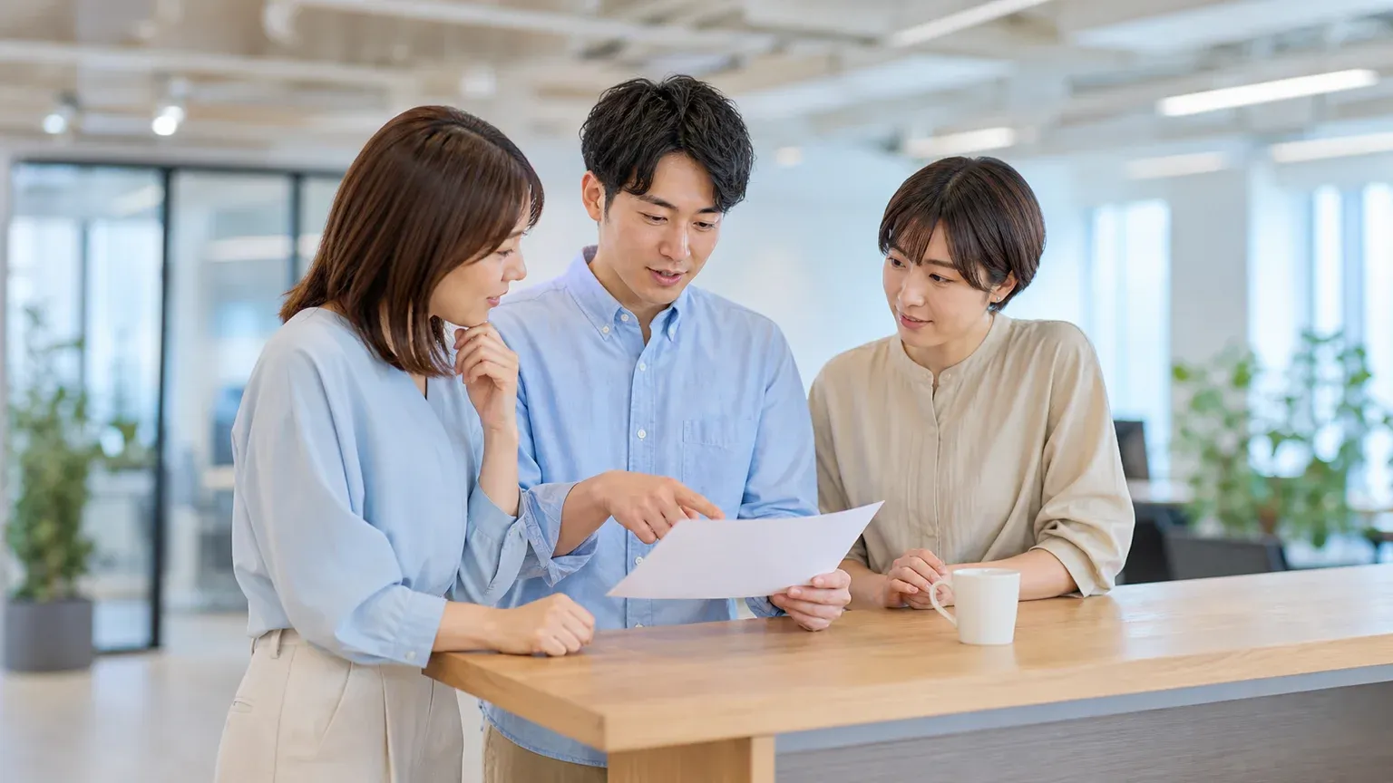 オープンオフィスで資料を見ながら生成AIの活用事例を共有する3人の社員
