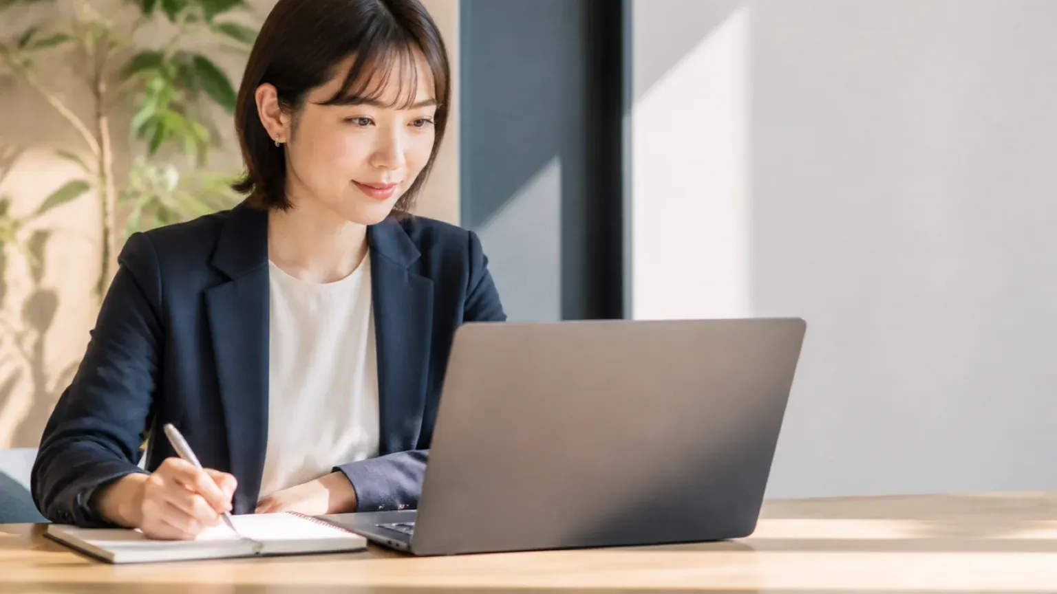 明るいオフィスで30代女性の担当者がノートPCの画面を見ながら、外部の保守会社に依頼する範囲を手元のノートに書き出している場面