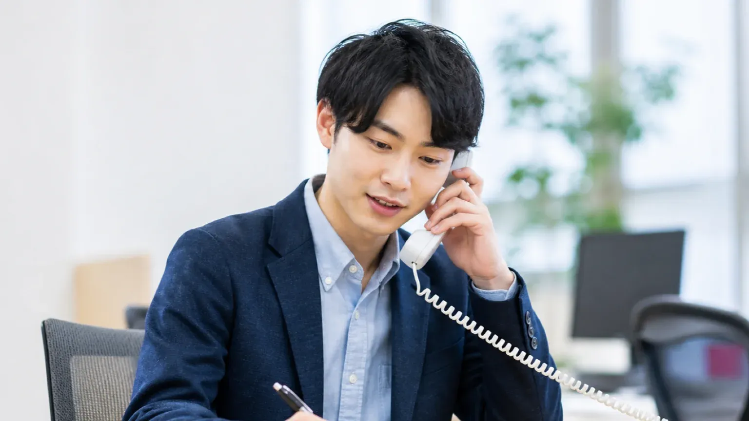 不動産会社で電話の問い合わせ内容をメモに書き取る営業担当者