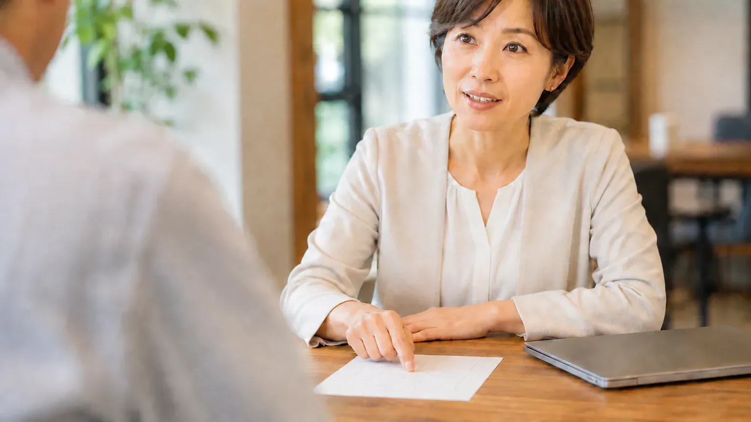 打ち合わせのテーブルで、担当者が手元の資料に指を添えながら業務側の条件を伝えている場面