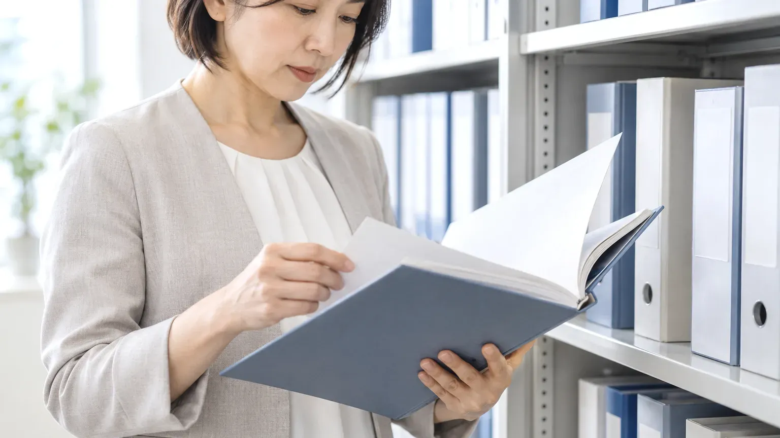 書庫のキャビネットから綴じた契約書類を1冊取り出して開き、条件を確かめている手元