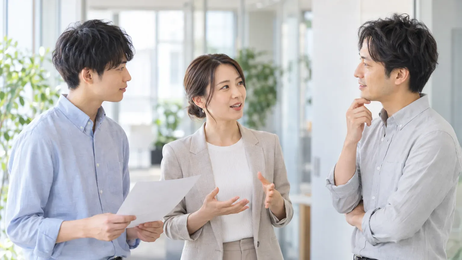 オフィスの一角で3人が輪になって立ち話し、1人が手振りを交えて条件を説明している場面