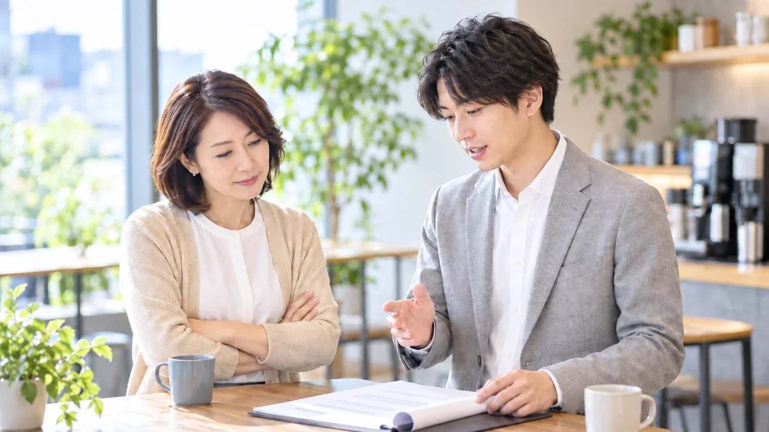 休憩スペースのハイテーブルで、経理の担当者と情報システムの担当者が契約書の控えを前に印紙の扱いを話している様子