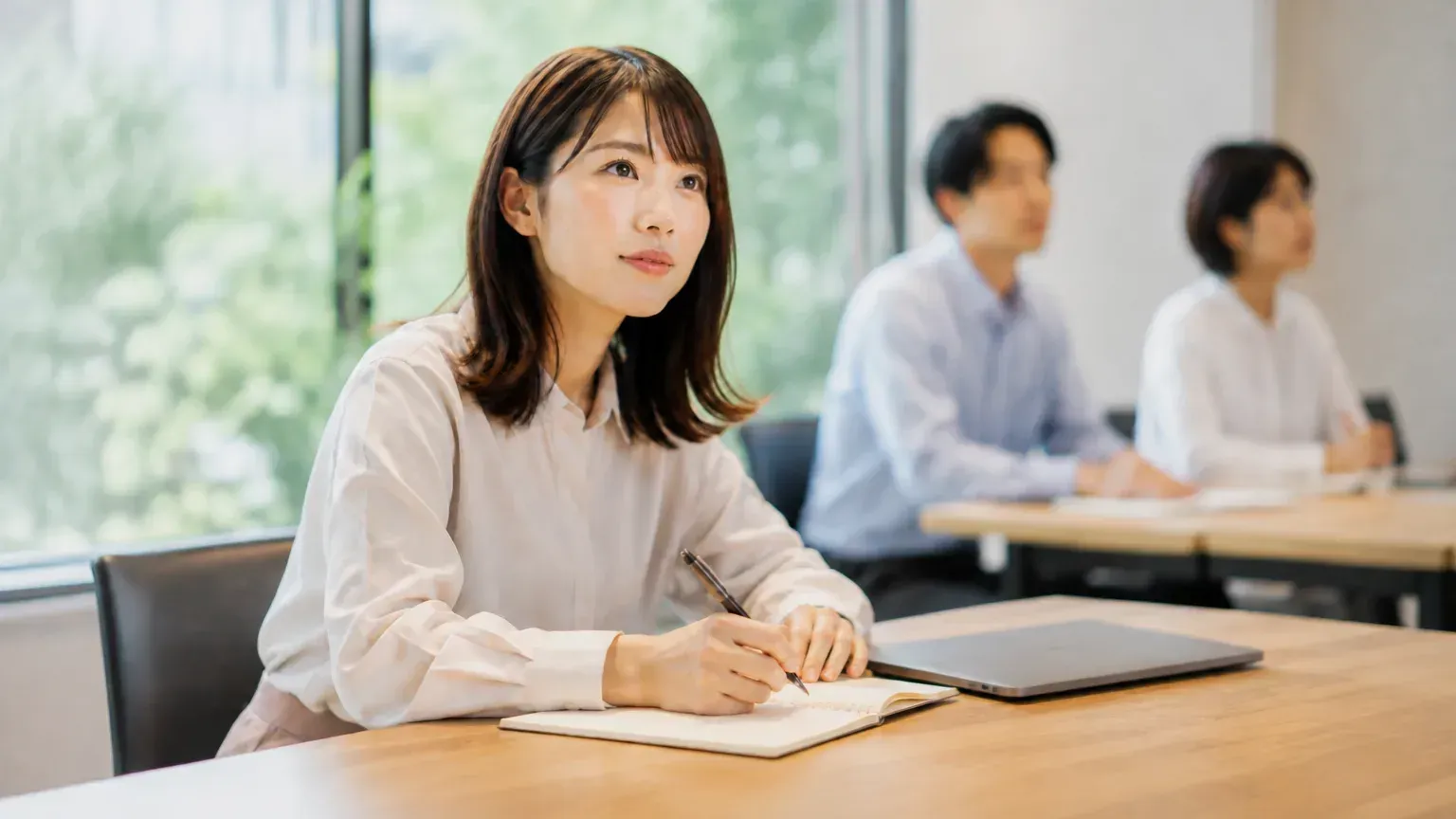 会議室で発言を聞きながら、担当者が手元のノートに決まったことを書き留めている場面