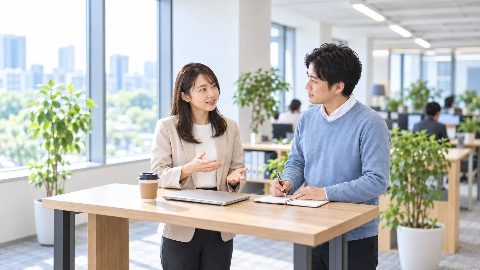 立ち話のスペースで、情報システムの担当者が開発会社の担当者から個人データの取扱いについて説明を受け、メモを取っている様子