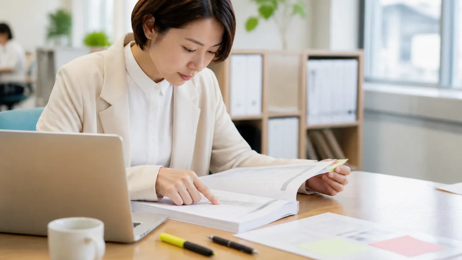 デスクで分厚い計画書のページをめくりながら、担当者が指で行を追って内容を確かめている場面