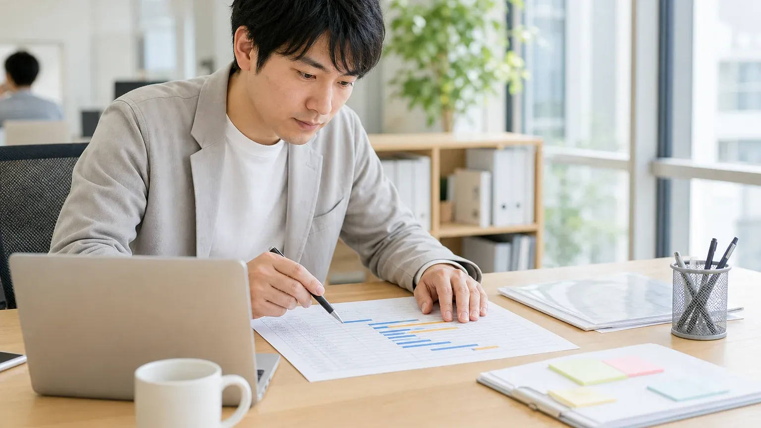 デスクに広げた作業一覧表を、担当者がペン先で行を追いながら確認している場面